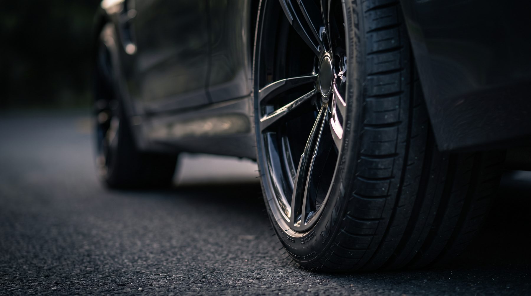 Low angle close-up of a performance tyre and black alloy wheel on tarmac